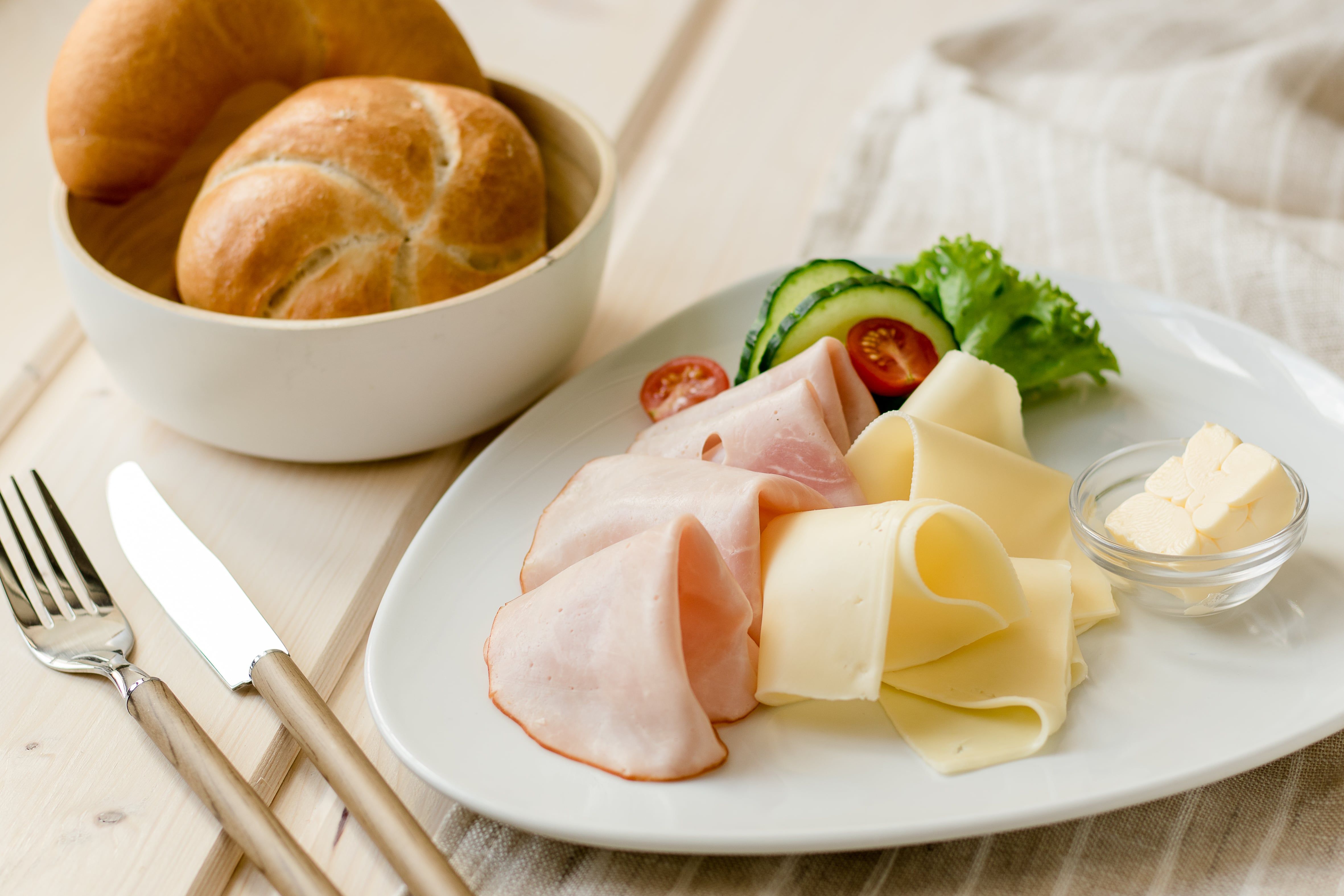 Frühstücksteller mit Schinken, Käse, Gurken, Tomaten und Brötchen.