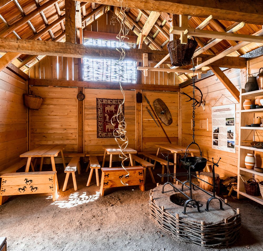 Rekonstruktion eines keltischen Dorfes mit Holzhütten und grünem Rasen, umgeben von Bäumen.