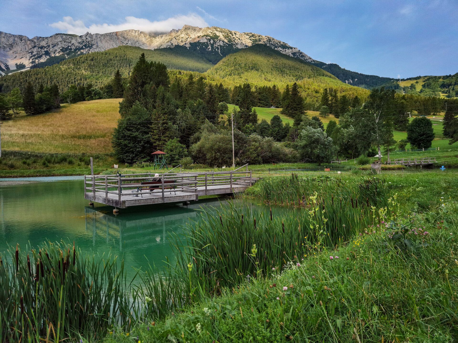 Die sanften Hügel und der glitzernde Teich laden zu einem entspannten Tag in der Natur ein. Umgeben von majestätischen Bergen, bietet dieser Ort eine perfekte Kulisse für Wanderer und Naturliebhaber. Hier kann man die frische Bergluft genießen und die Ruhe der Landschaft erleben.
