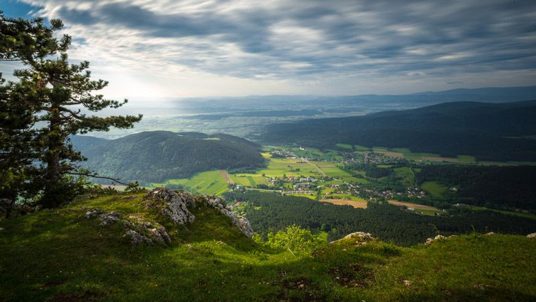 Blick von einer Felskante auf eine grüne Landschaft mit Hügeln und einem Dorf im Tal.