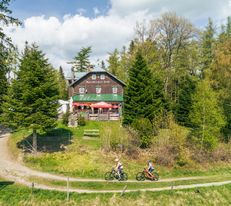 Holzhütte mit der Aufschrift "Speckbacherhütte", rundherum Bäume und zwei Mountainbikefahrer davor