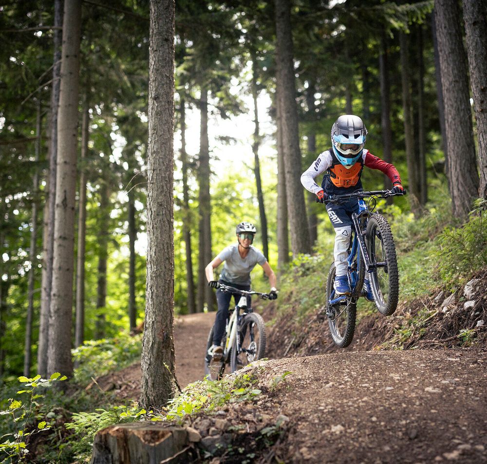 Kind und Erwachsener fahren mit Mountainbikes auf einem angelegten Waldtrail im Alpenbikepark Puchberg am Schneeberg in Niederösterreich, umgeben von dichtem Nadelwald in den Wiener Alpen.