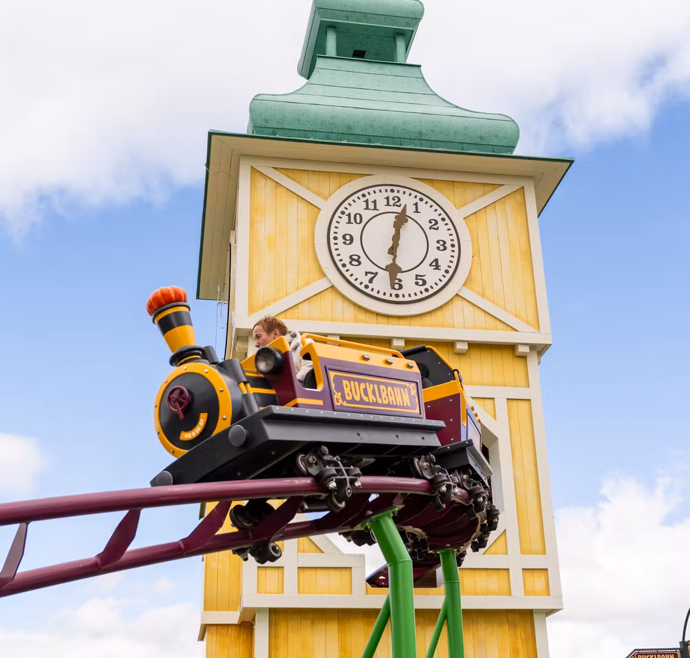 Eine Waggon der Achterbahn Bucklbahn im Eis-Greissler Erlebnispark, im Hintergrund gelber Turm mit Uhr.