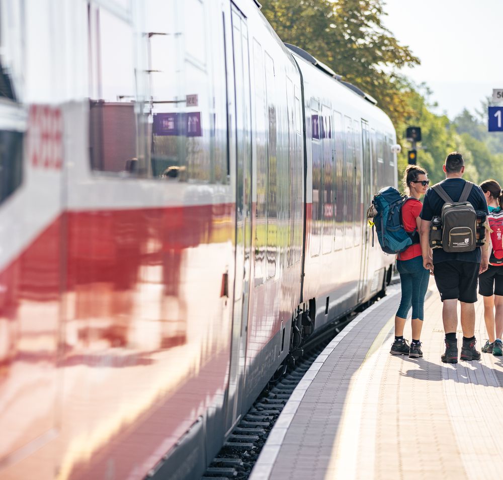 Wanderer am Bahnsteig mit Zug in der Station stehend