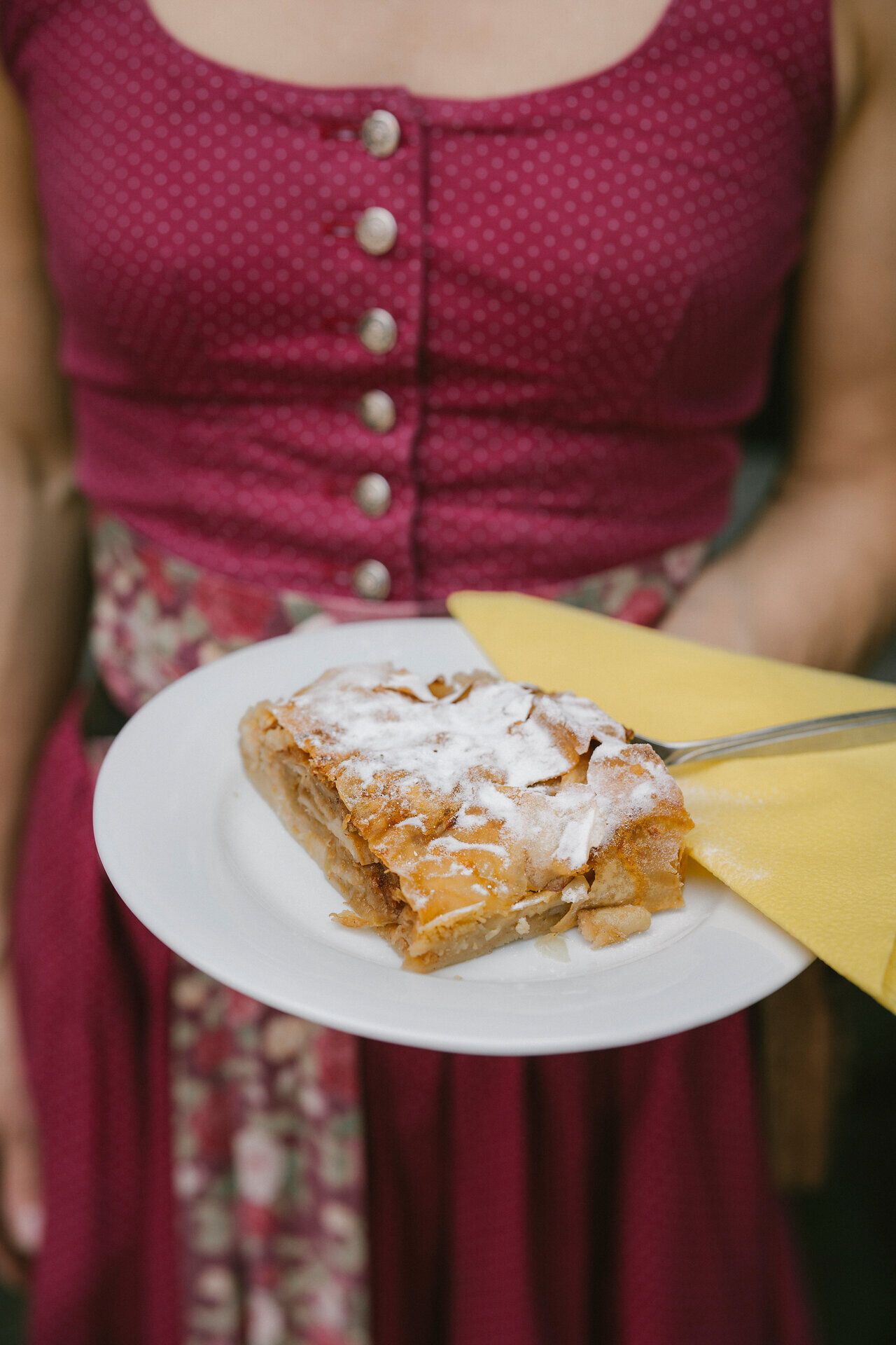 Mitarbeiterin im Dirndl präsentiert ein Stück Apfelstrudel in der Hengsthütte am Schneeberg