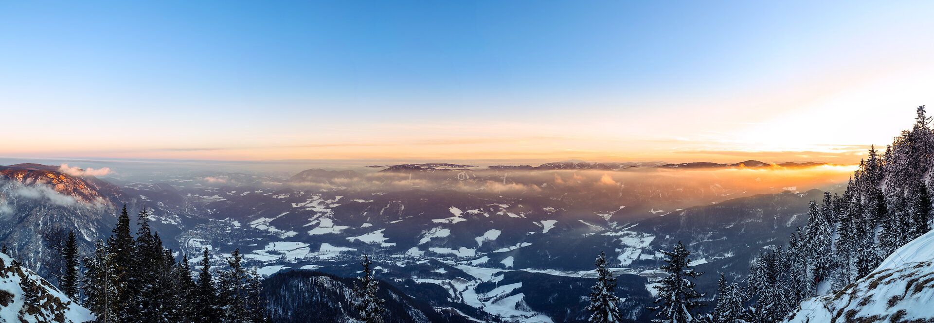 Panoramablick von der Rax ins verschneite Tal, die untergehende Sonne färbt das Tal orange.