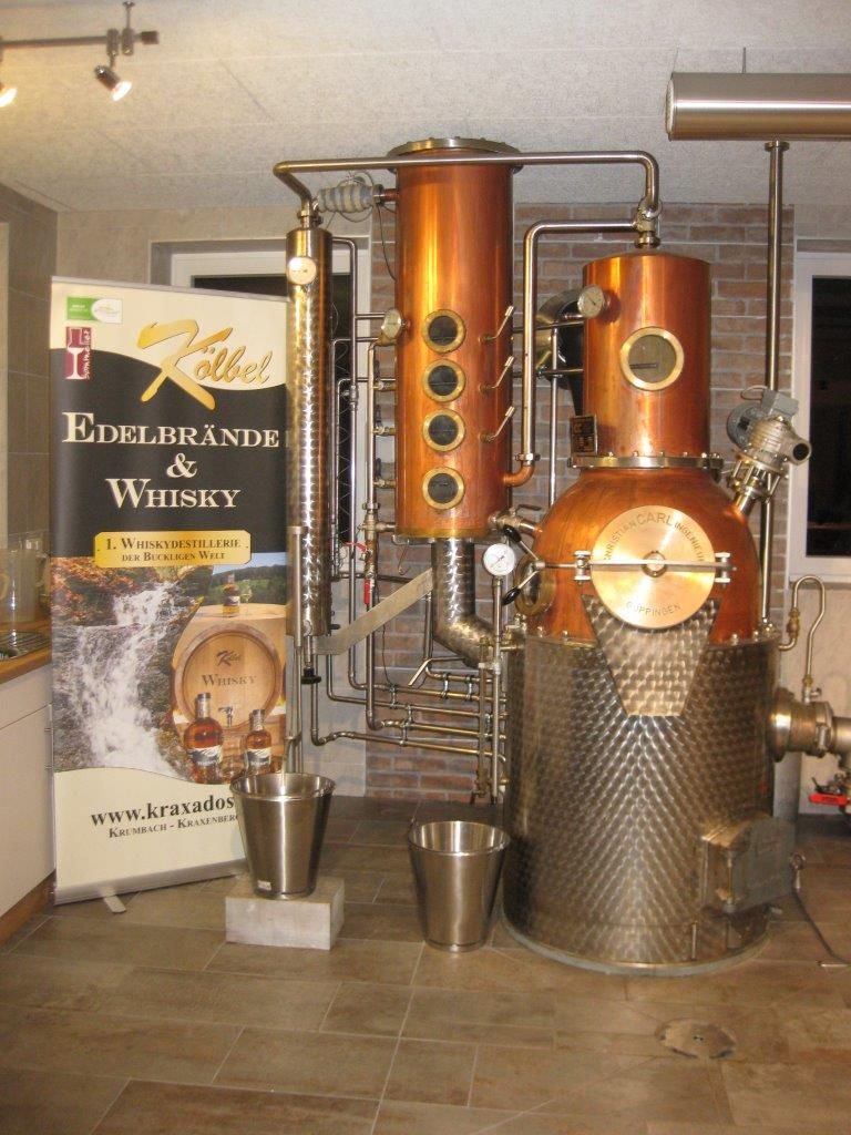 Eine Schnapsbrennanlage in einer Brennerei, daneben ein Rollup der Brennerei Kölbel.