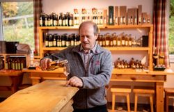 Mann steht an einer Theke aus Holz und gießt Schnaps in ein Schnapsglas.