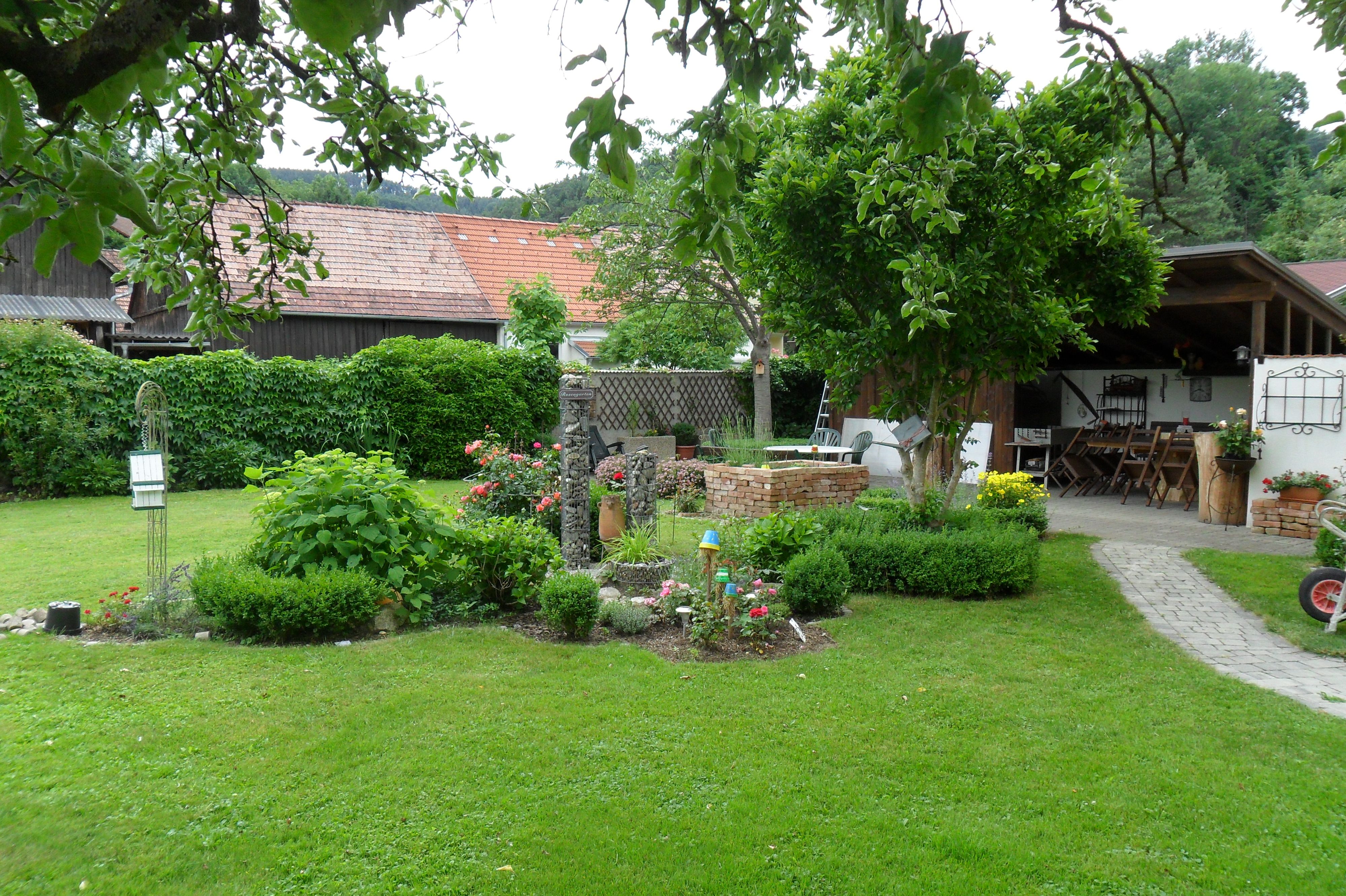Garten mit Rasen, Blumenbeeten und überdachtem Sitzbereich.