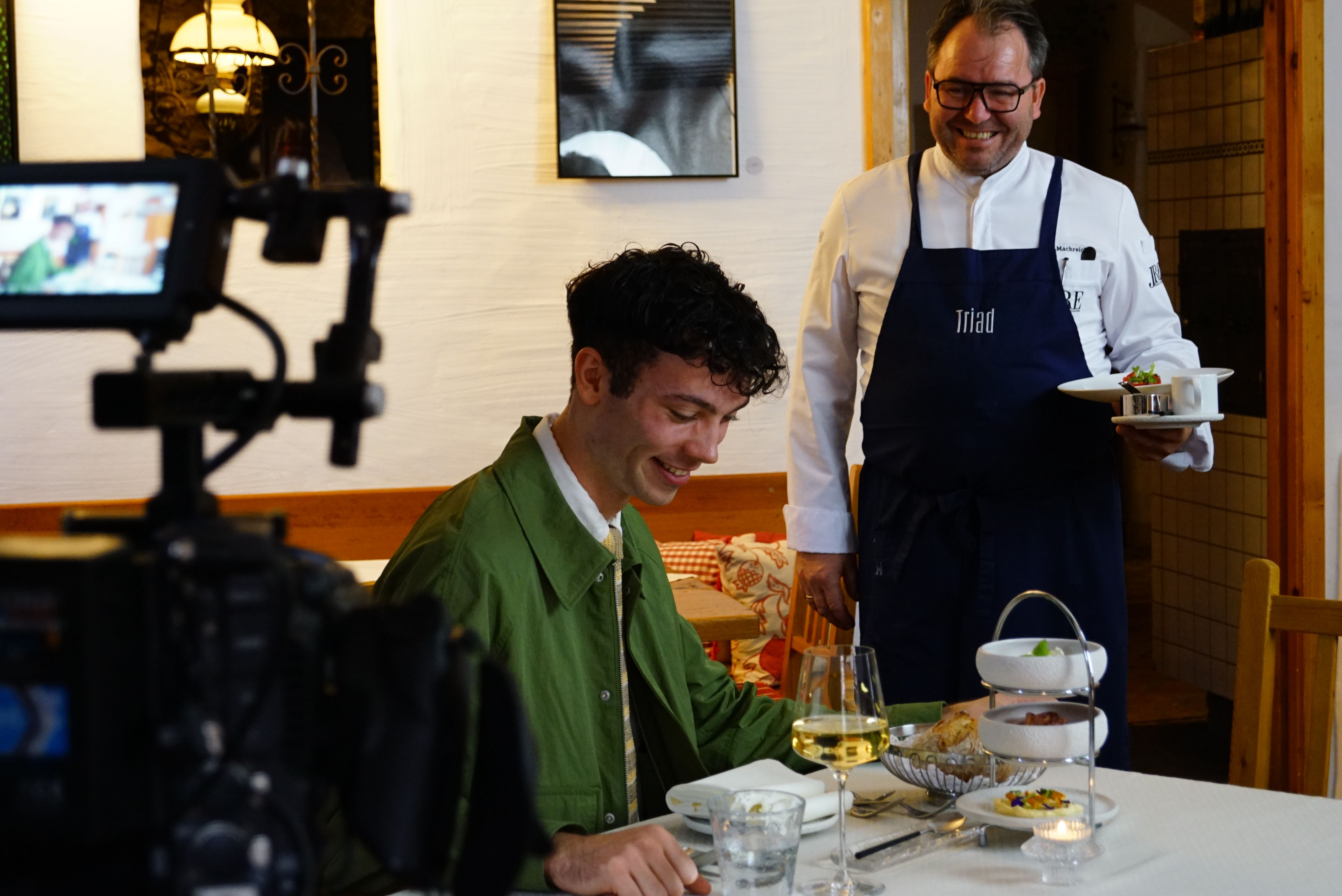 Ein junger Mann, der am Tisch gerade eine Speise vom Triad-Chef Uwe Machreich serviert bekommt, wird dabei gefilmt.