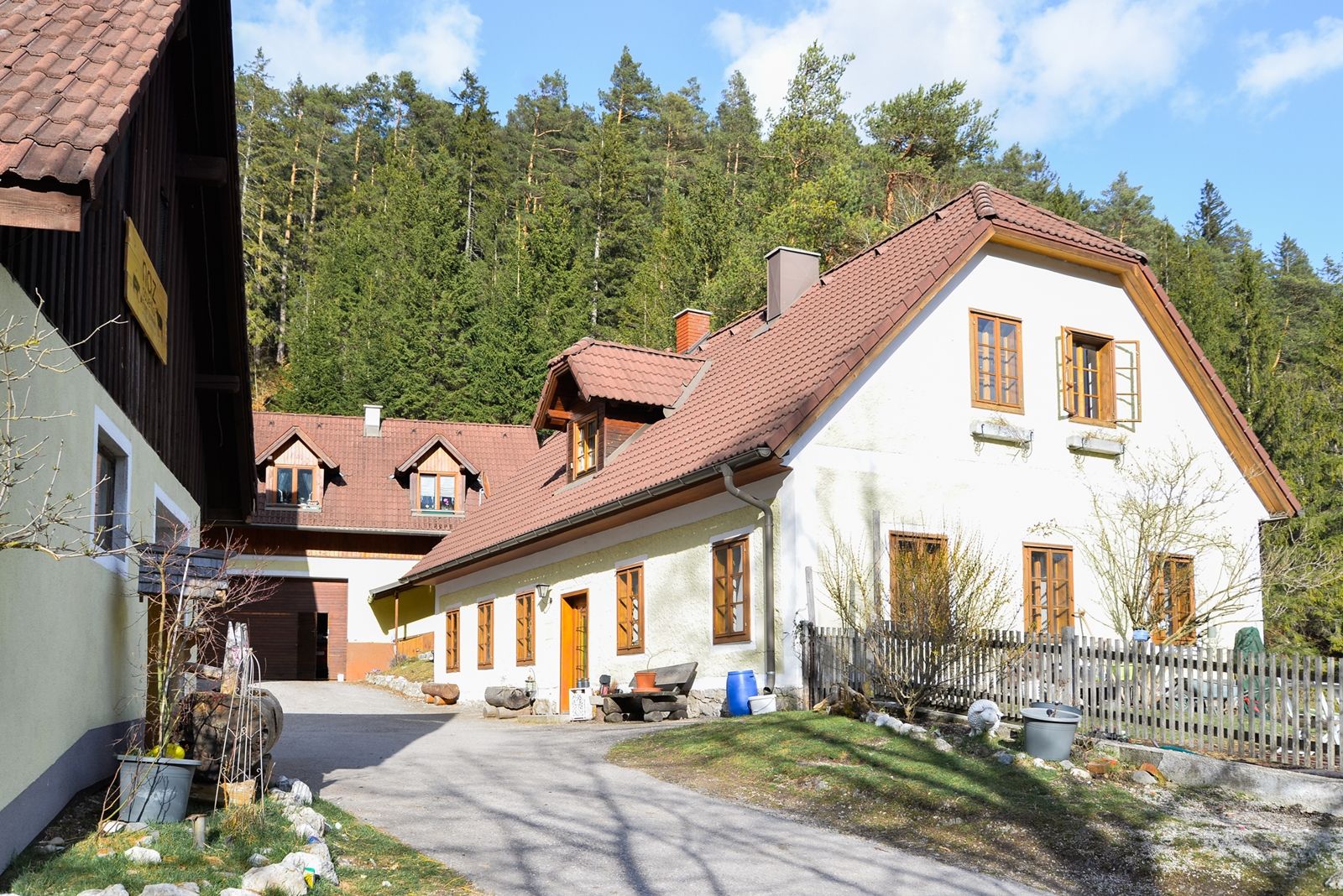 Ein traditionelles Bauernhaus mit roten Dächern vor einem Wald.