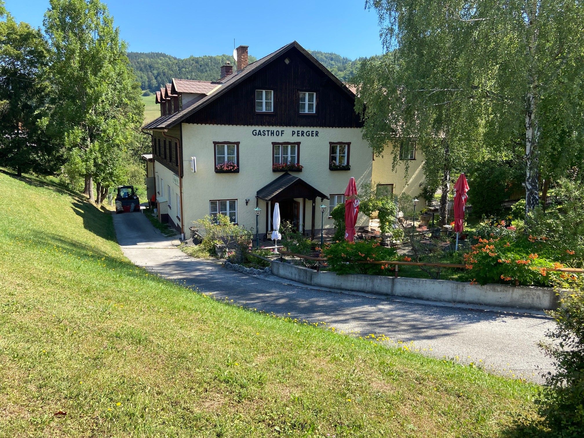 Ein traditionelles Gasthaus mit Terrasse und Sonnenschirmen, umgeben von grüner Landschaft.