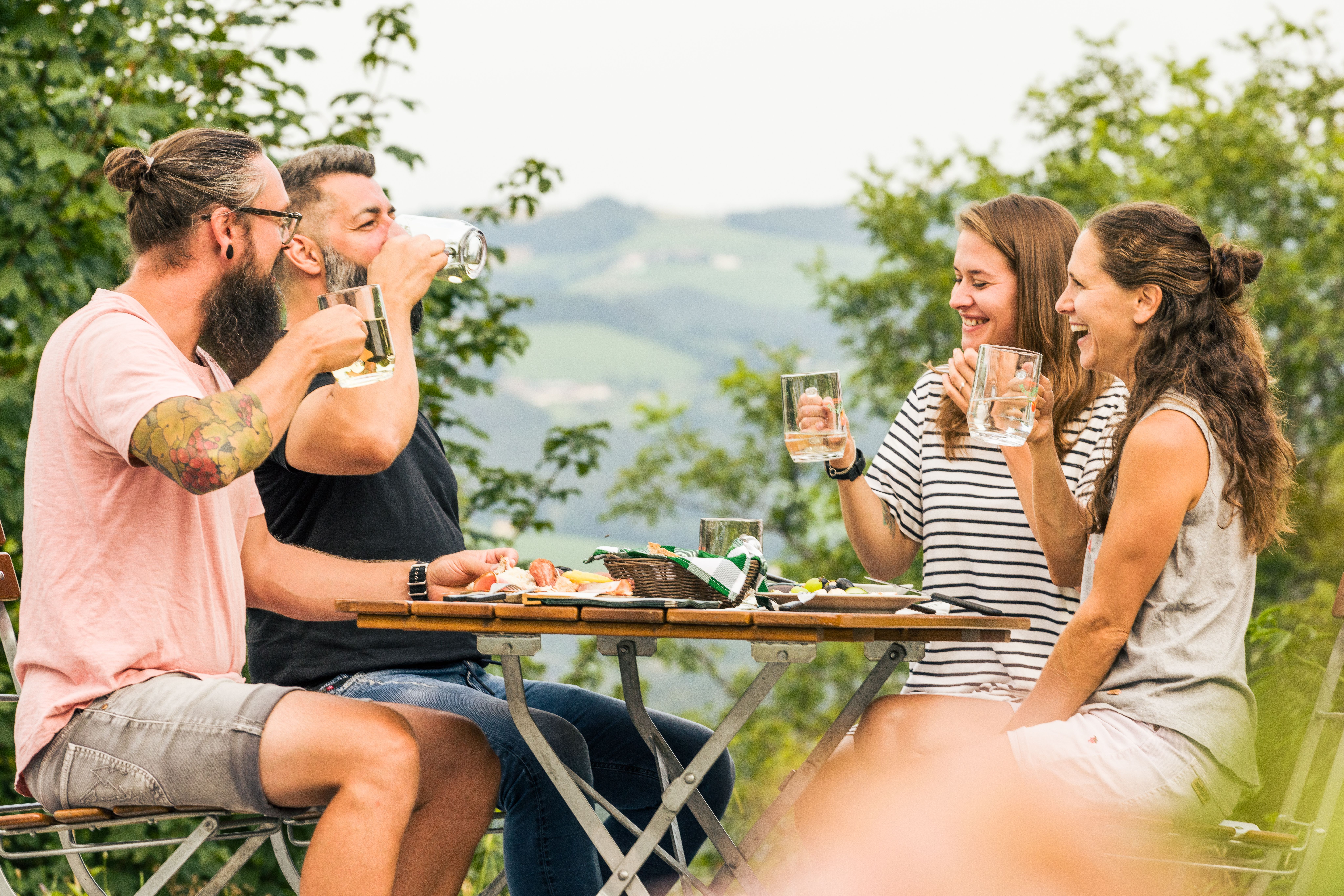 Vier Personen sitzen an einem Tisch im Freien, jeder hält ein Mostglas in der der Hand.