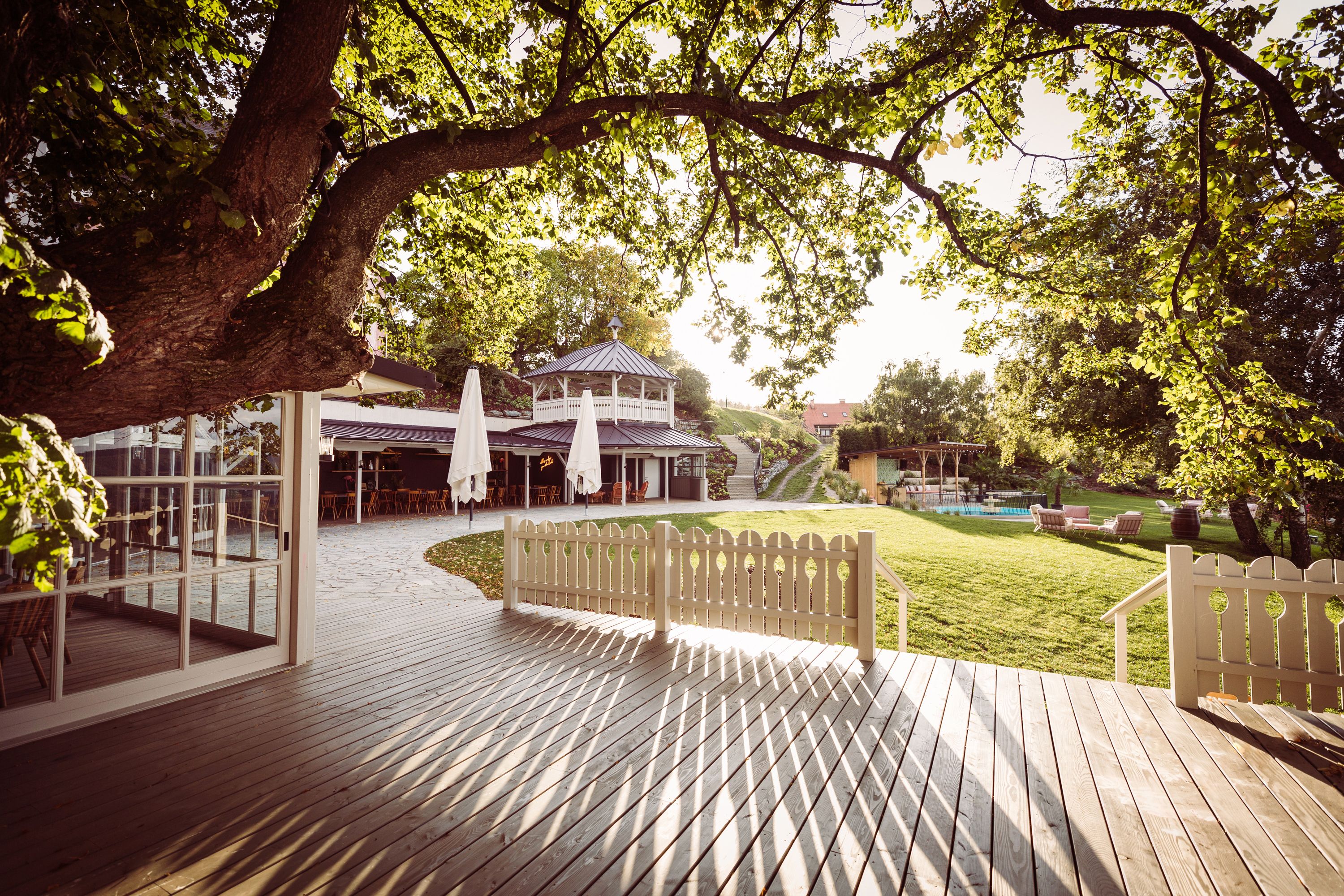 Ein Garten mit Terrasse, Bäumen und einem Pavillon im Sonnenlicht.