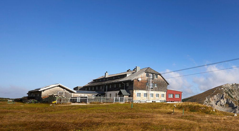 Panoramablick auf einen Berghütte mit umliegenden Gipfeln unter blauem Himmel.