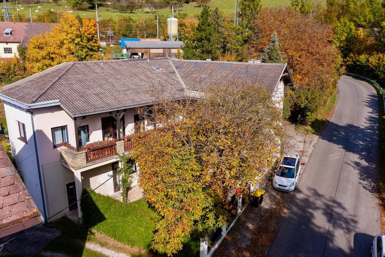 Luftaufnahme eines zweistöckigen Gebäudes mit Balkon, umgeben von herbstlichen Bäumen und einer Straße.
