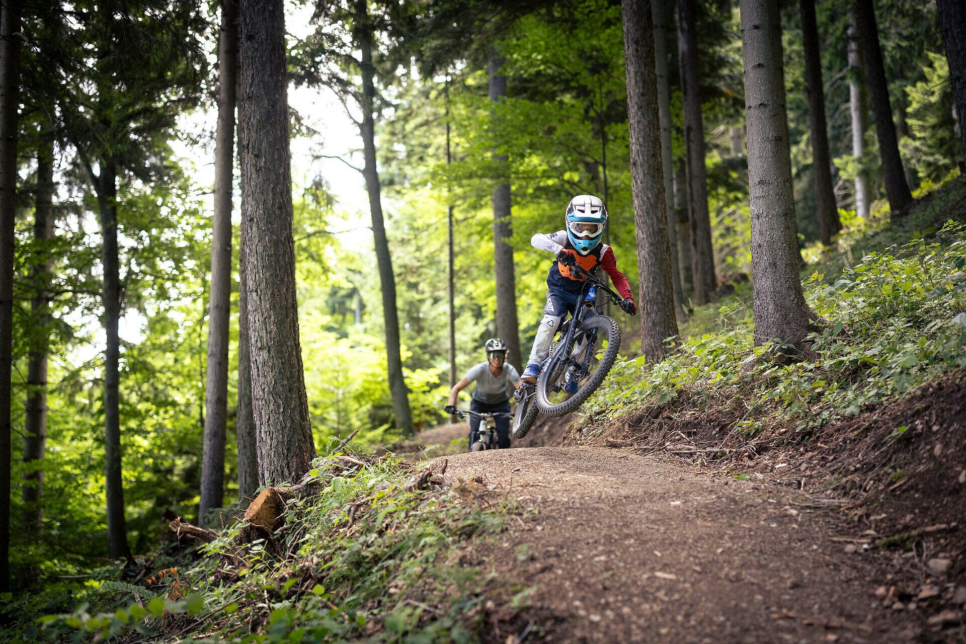 Familienfreundliches Mountainbike-Erlebnis auf einem Waldtrail in Puchberg am Schneeberg in Niederösterreich: Kind und Erwachsener fahren gemeinsam auf einem naturnahen Singletrail durch den grünen Alpenwald der Wiener Alpen.