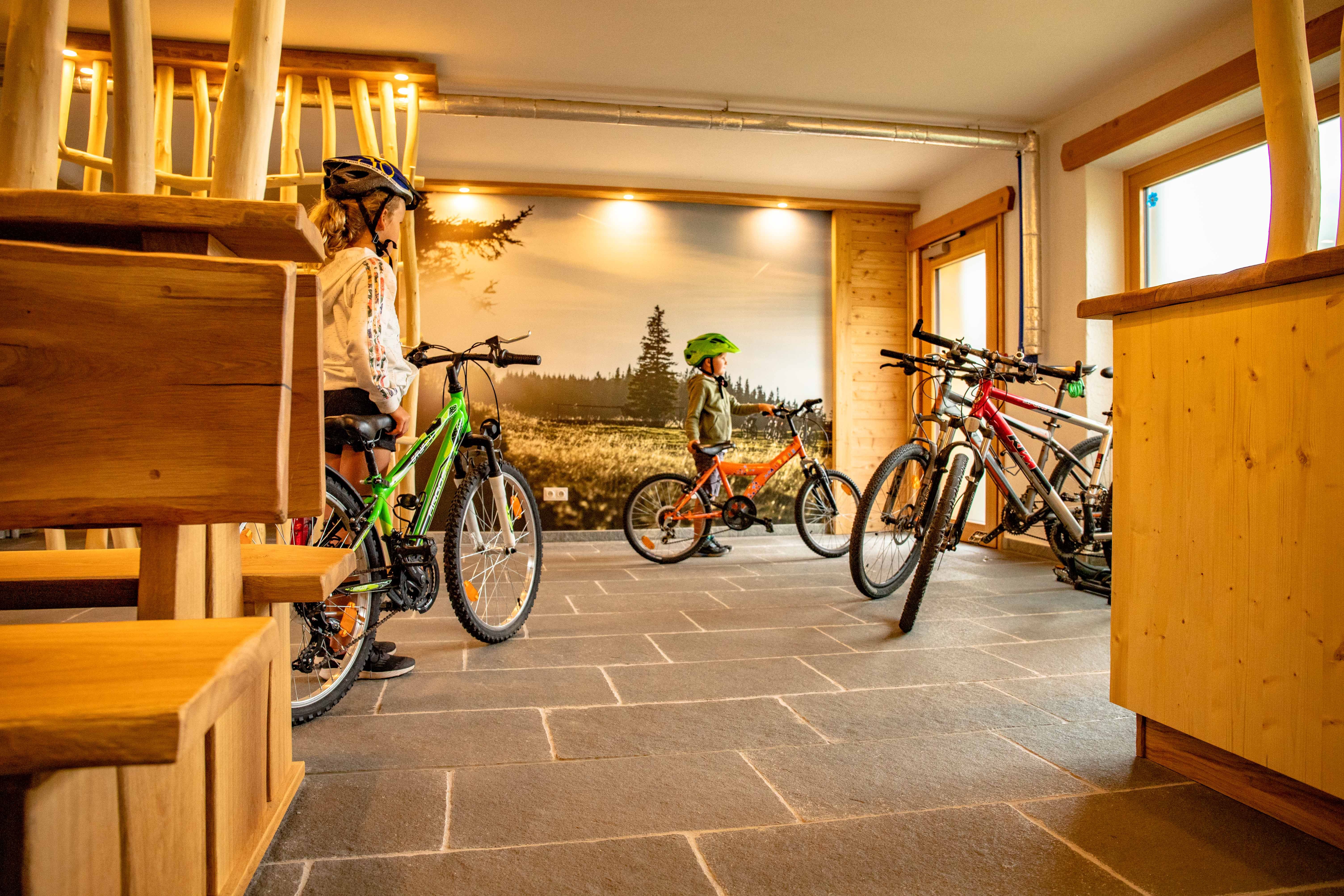 Kinder mit Fahrrädern in einem Raum mit Holzmöbeln und Landschaftsfototapete.
