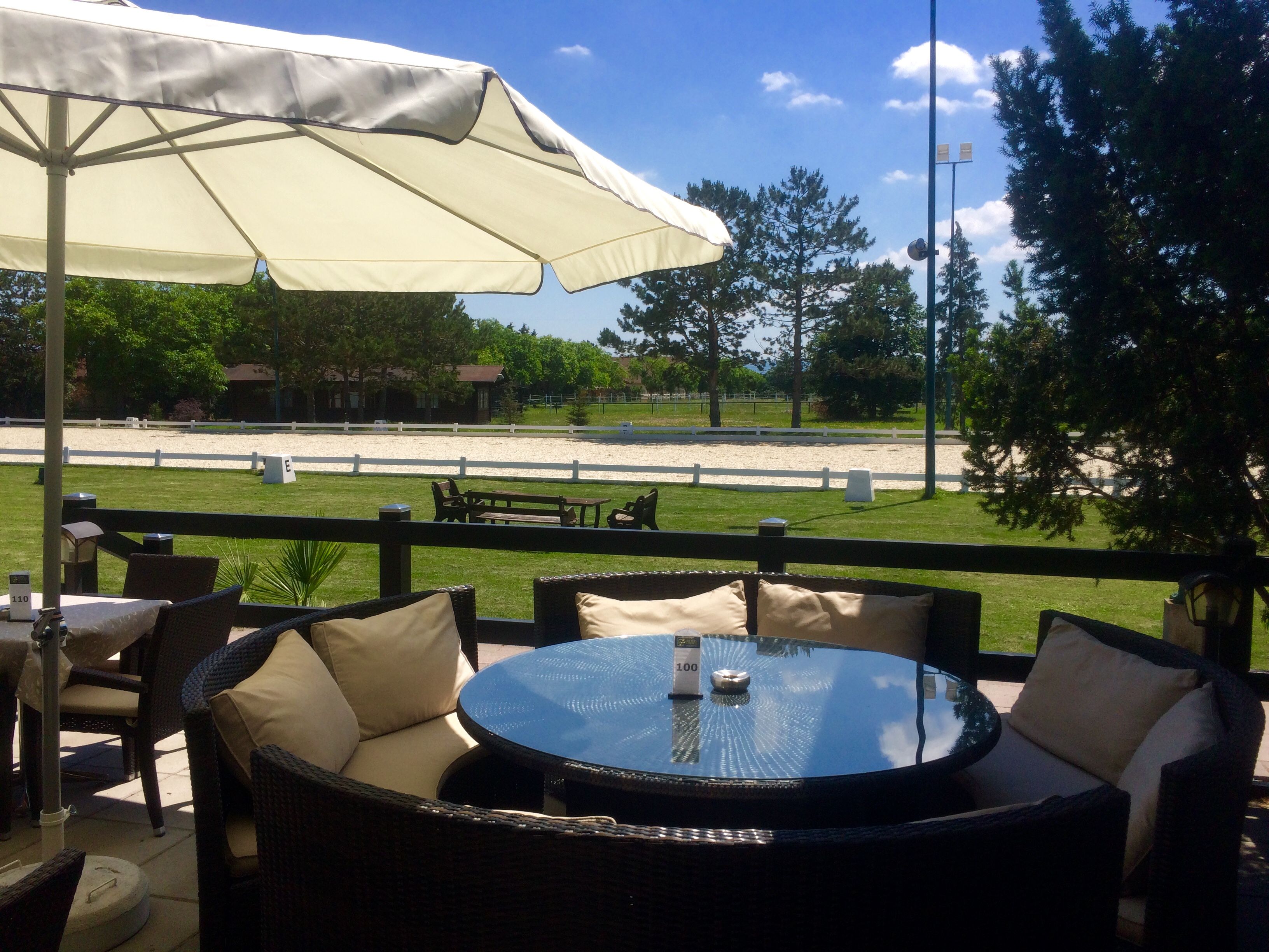 Terrasse mit runden Sitzgelegenheiten und Blick auf einen Reitplatz.