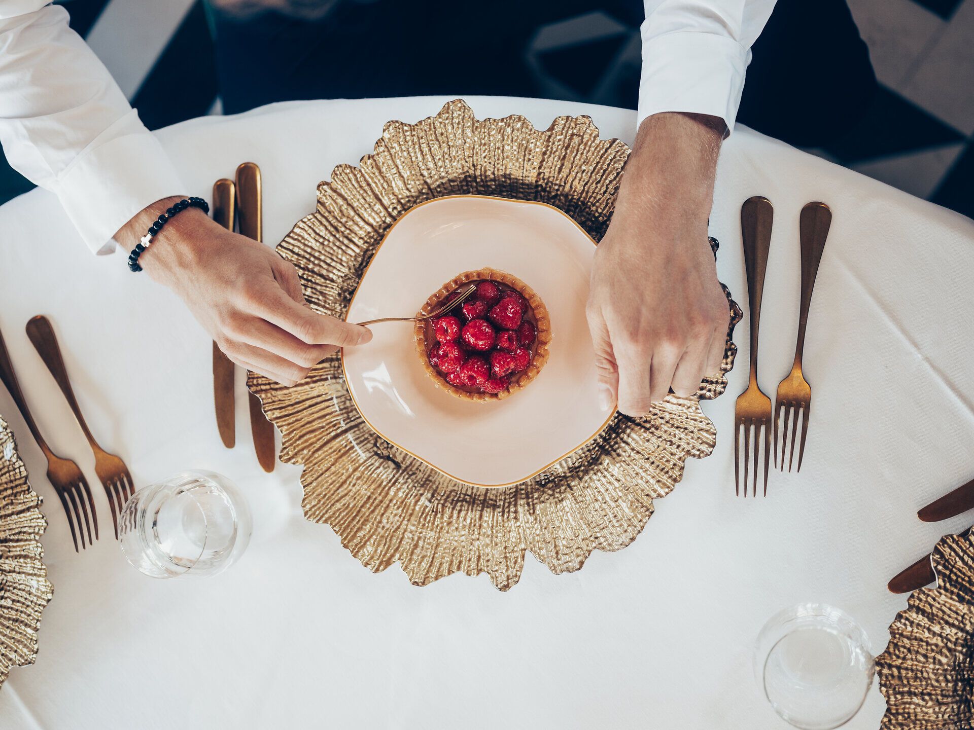 Ein köstliches Dessert wird liebevoll serviert, umgeben von elegantem Geschirr und goldenen Akzenten. Die frischen Himbeeren verleihen dem Gericht eine lebendige Farbe und laden dazu ein, den Moment in vollen Zügen zu genießen.