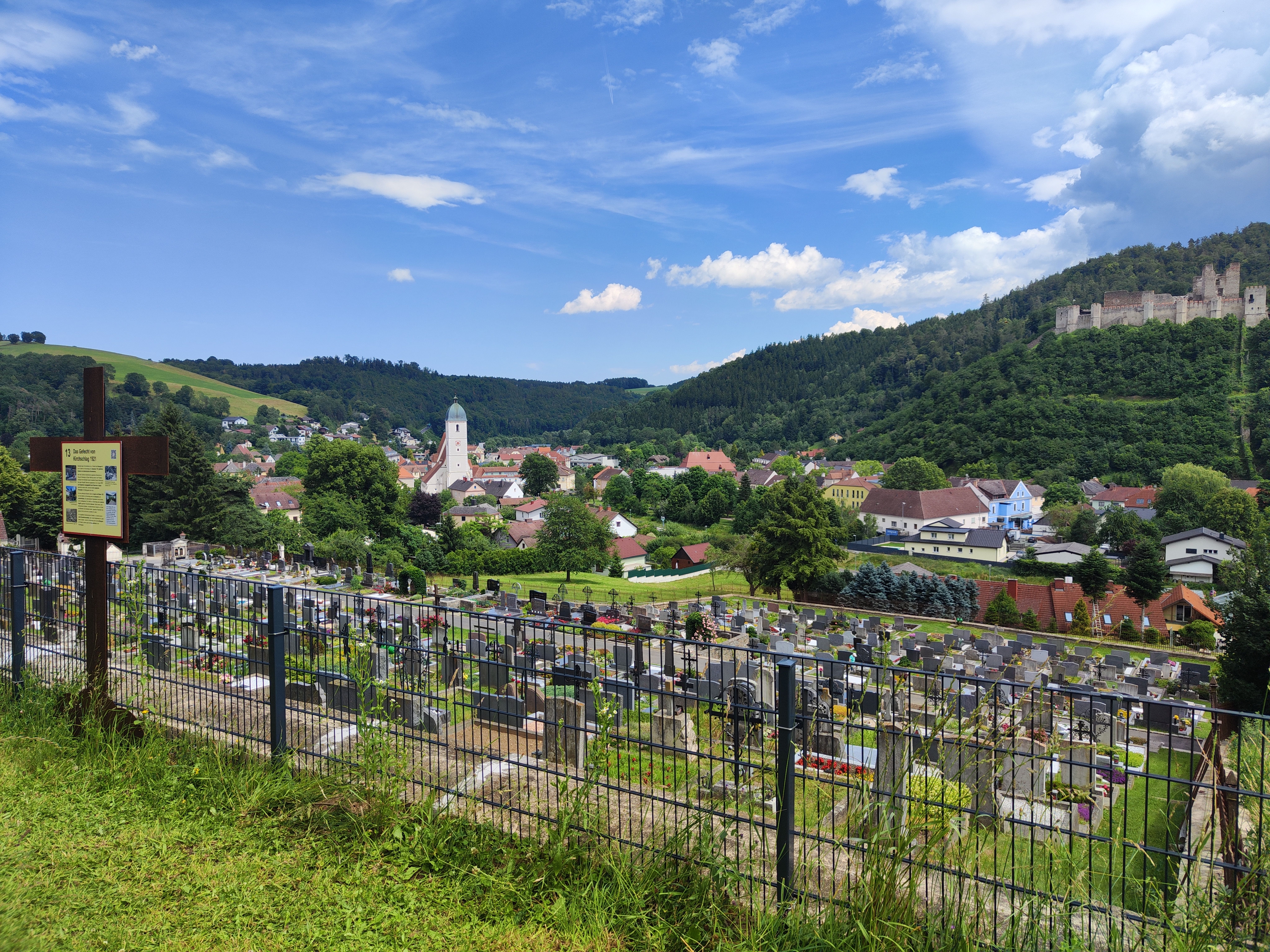 Blick auf Kirchschlag mit Friedhof im Vordergrund und Burgruine und Kirche im Hintergrund.