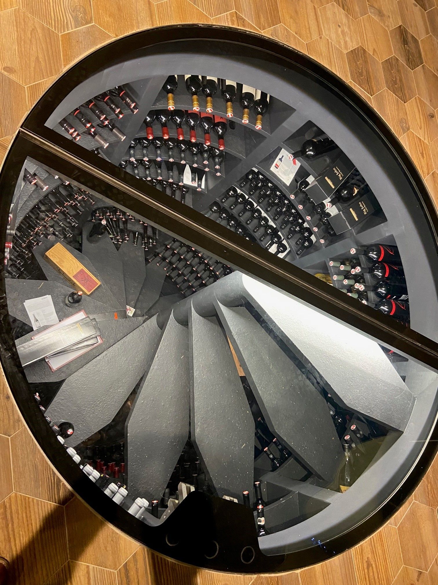 Blick durch eine Glasplatte auf einen spiralförmigen Weinkeller mit vielen Weinflaschen.