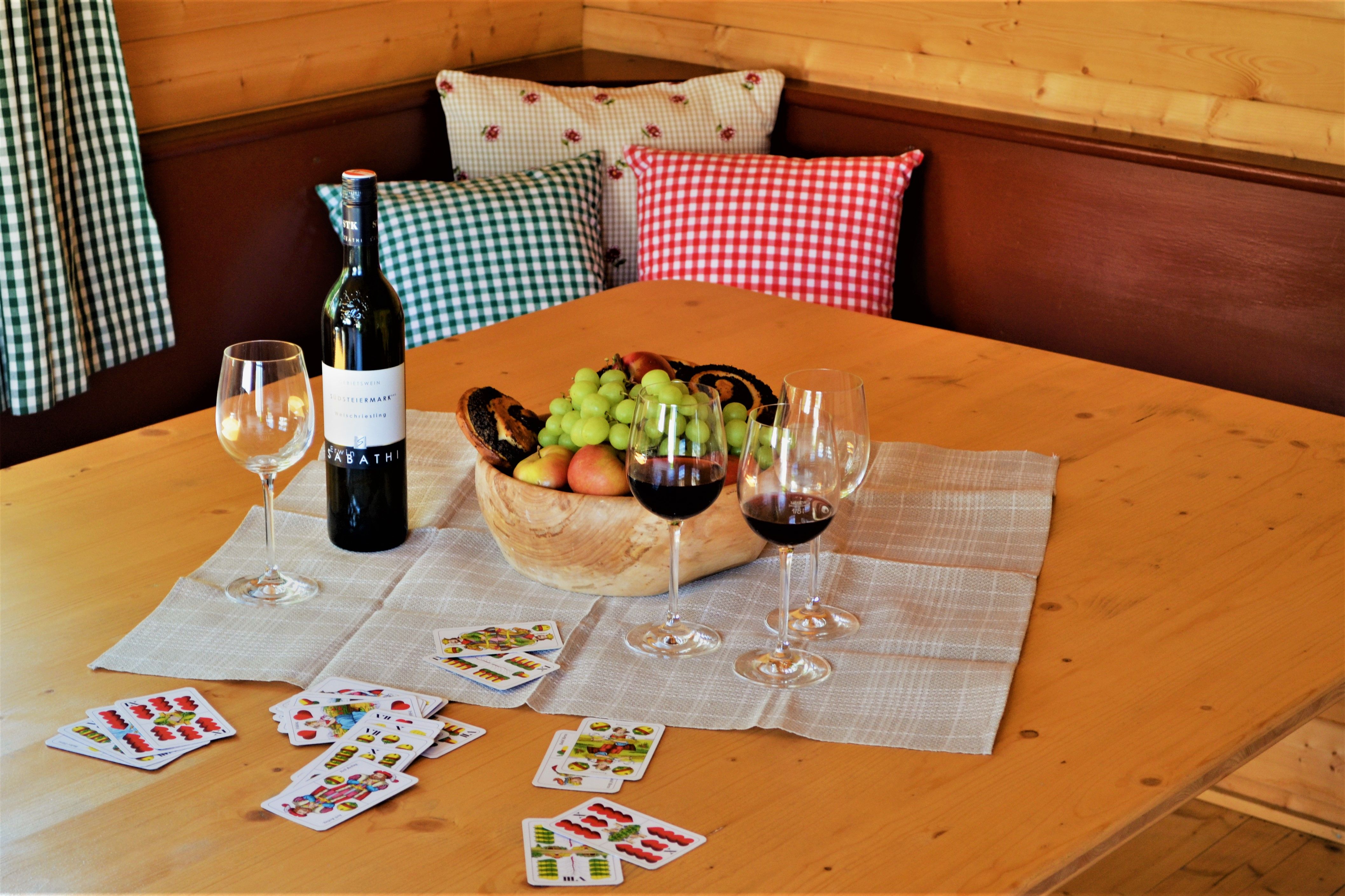 Ein Tisch mit Weinflasche, Weingläsern, Obstschale und Spielkarten.