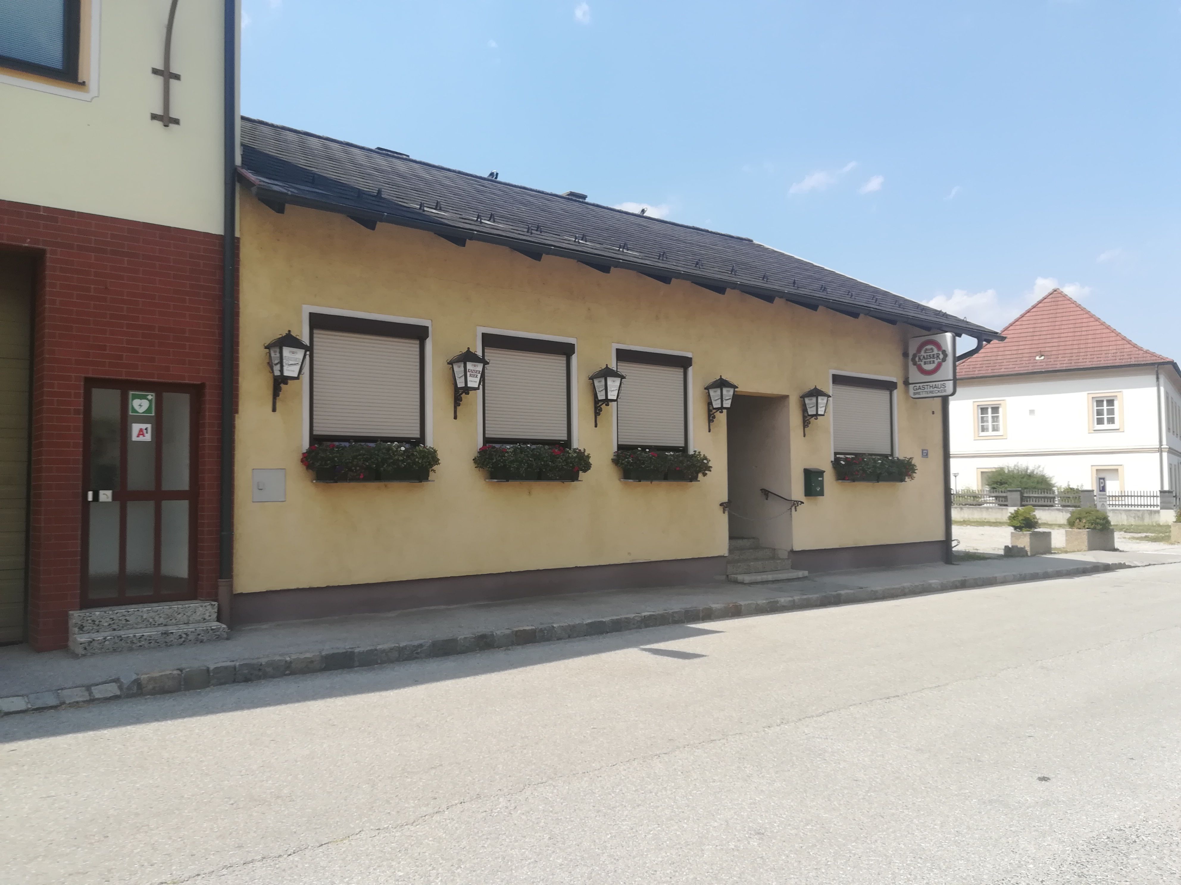 Außenansicht eines gelben Gasthauses mit geschlossenen Fensterläden und Blumenkästen.