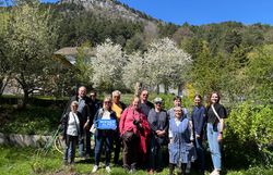 Eine Gruppe von rund 12 Personen steht in der Wiese in einem grünen Garten bei Sonnenschein. Eine Frau hält ein Wiener Alpen Logo-Schild in der Hand.