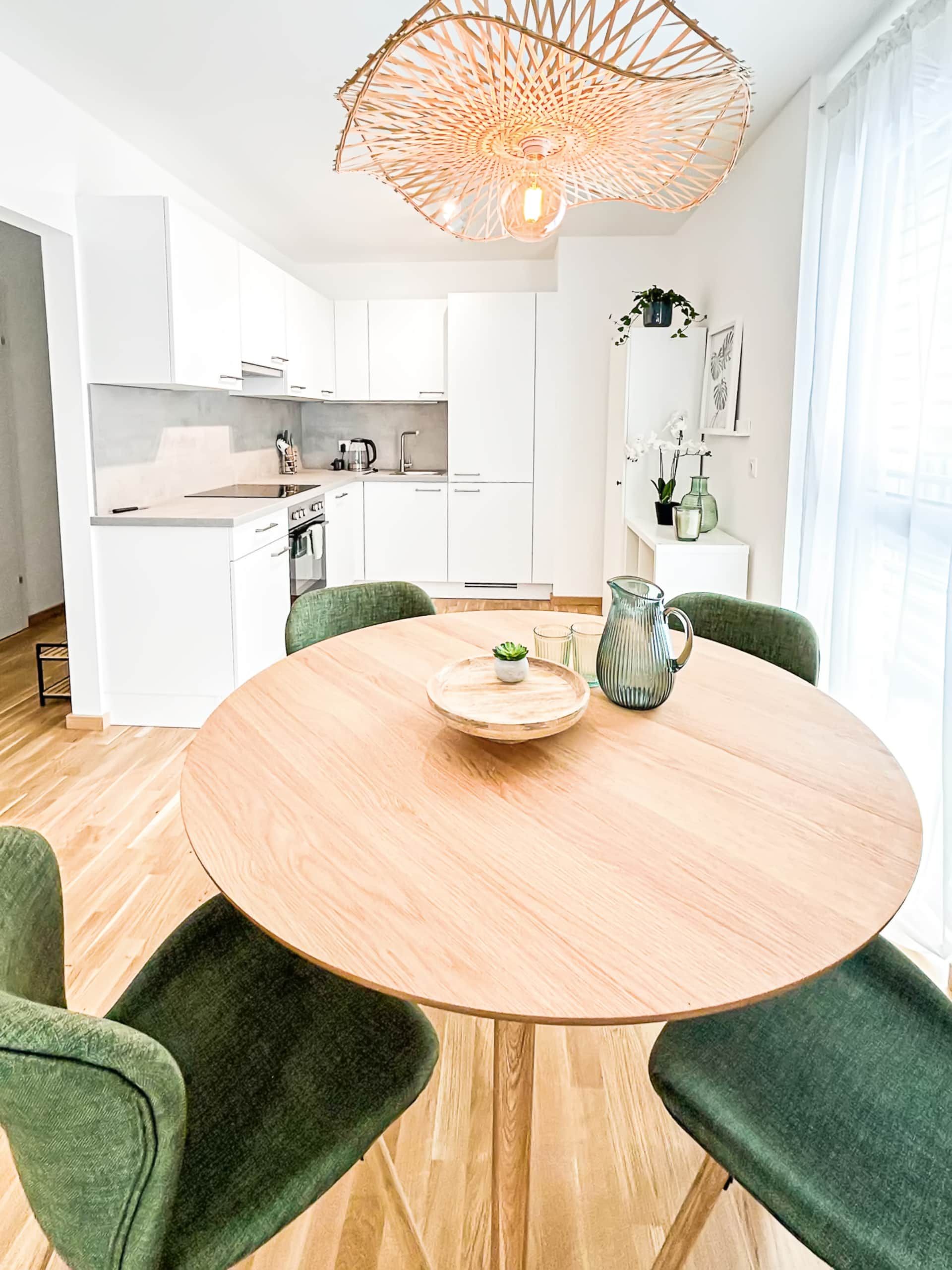Round dining table with green velvet chairs with a view of the large kitchen