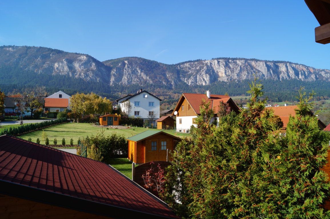 Blick auf Häuser mit roten Dächern und Berge im Hintergrund bei klarem Himmel.