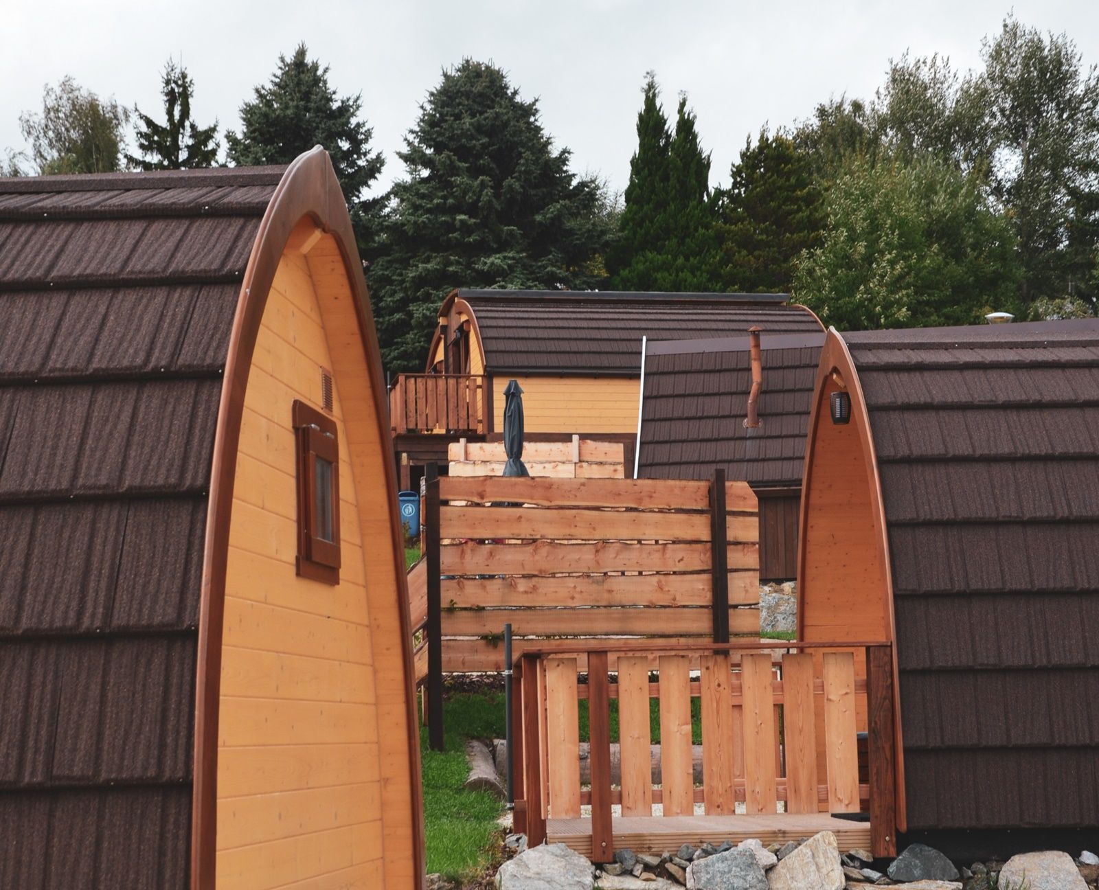 Mehrere hölzerne Glamping-Hütten mit braunen Dächern in einem bewaldeten Gebiet.