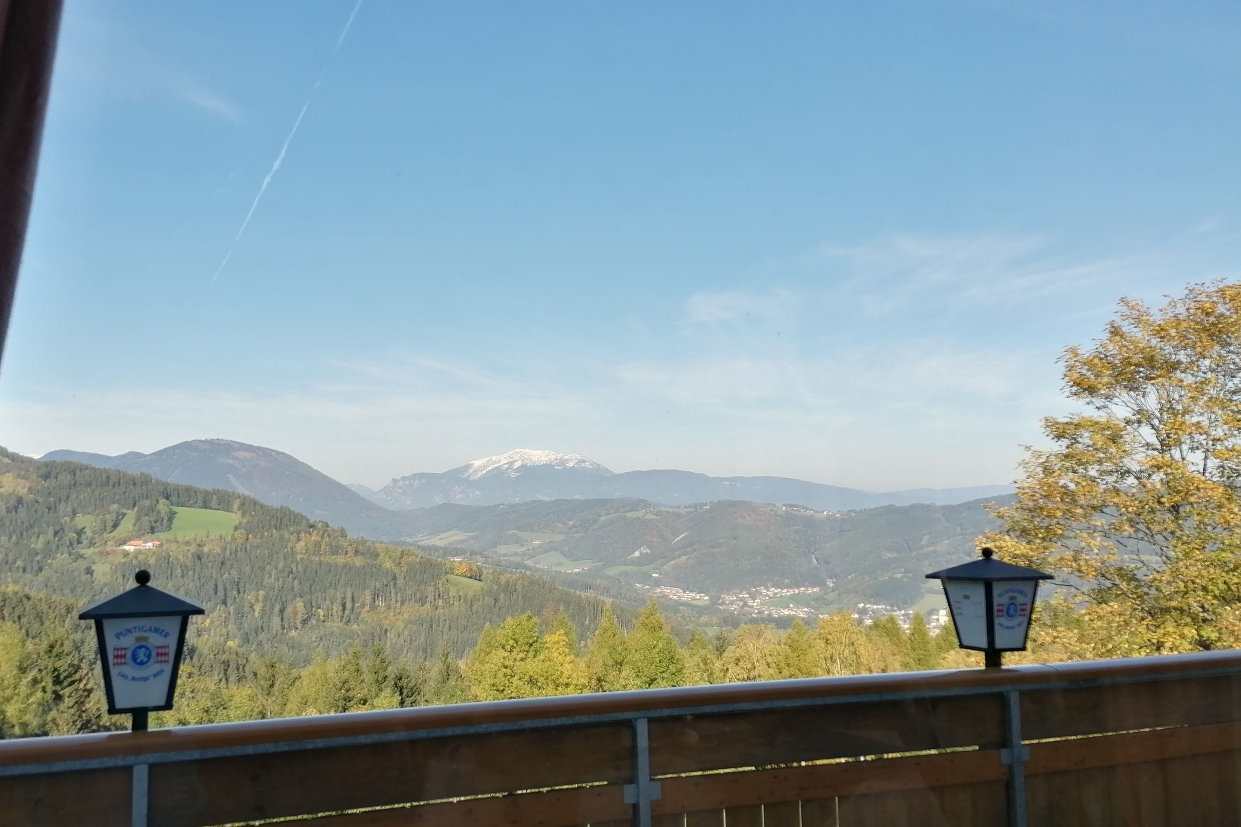 Blick von einem Restaurantbalkon auf eine bergige Landschaft mit Wald und einem schneebedeckten Gipfel im Hintergrund.