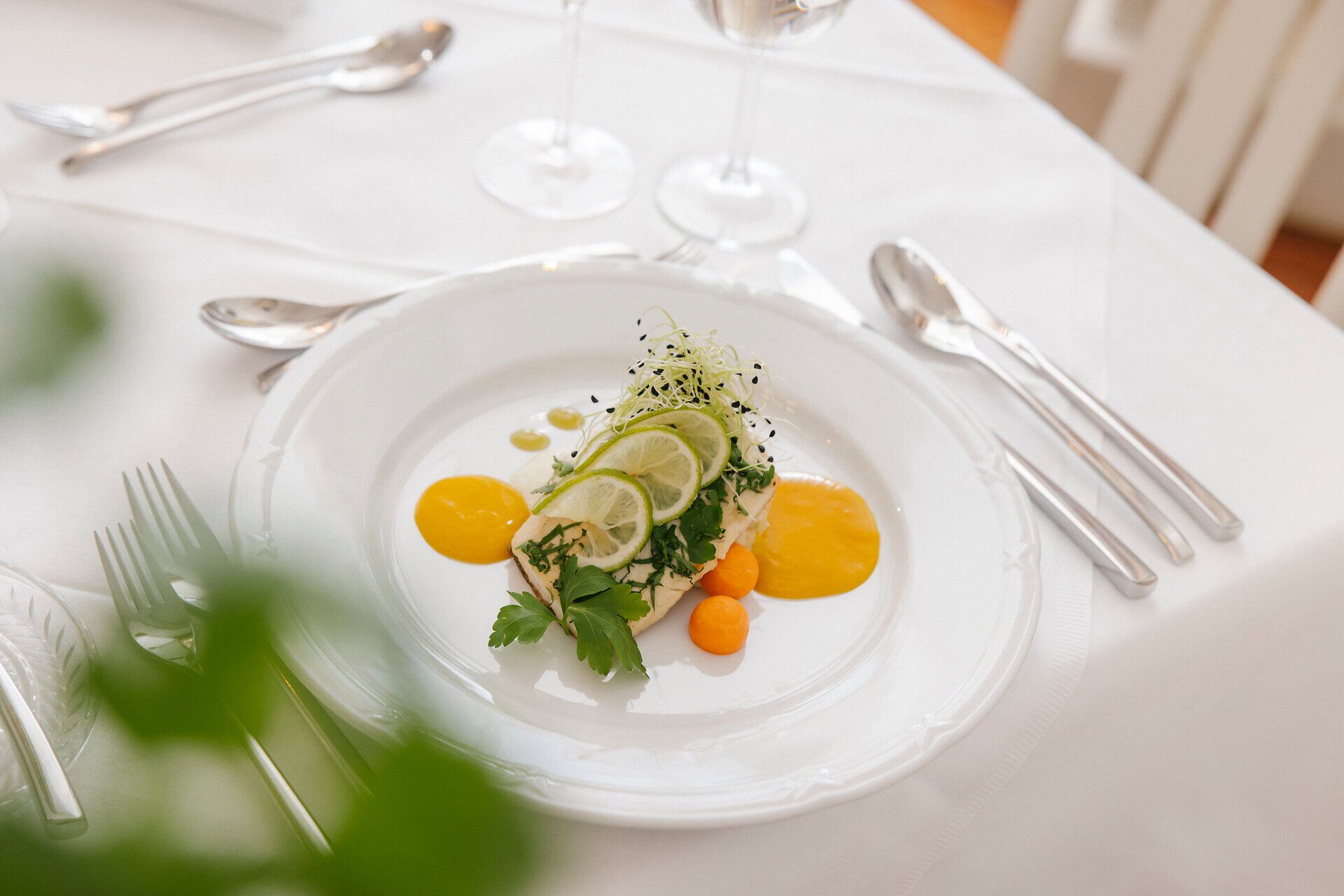 Fein angerichtetes Gericht auf einem weißen Teller auf einem schön gedeckten Tisch mit weißem Tischtuch.