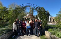 Eine Gruppe von rund 12 Personen steht im Stadtpark Wiener Neustadt vor dem Pavillon und einem Rosenbogen. Eine Frau hält ein Wiener Alpen Logo-Schild in der Hand.