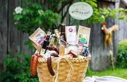 Geschenkkorb mit regionalen Lebensmitteln, im Hintergrund ein Holzzaun und ein Schnidahahn.