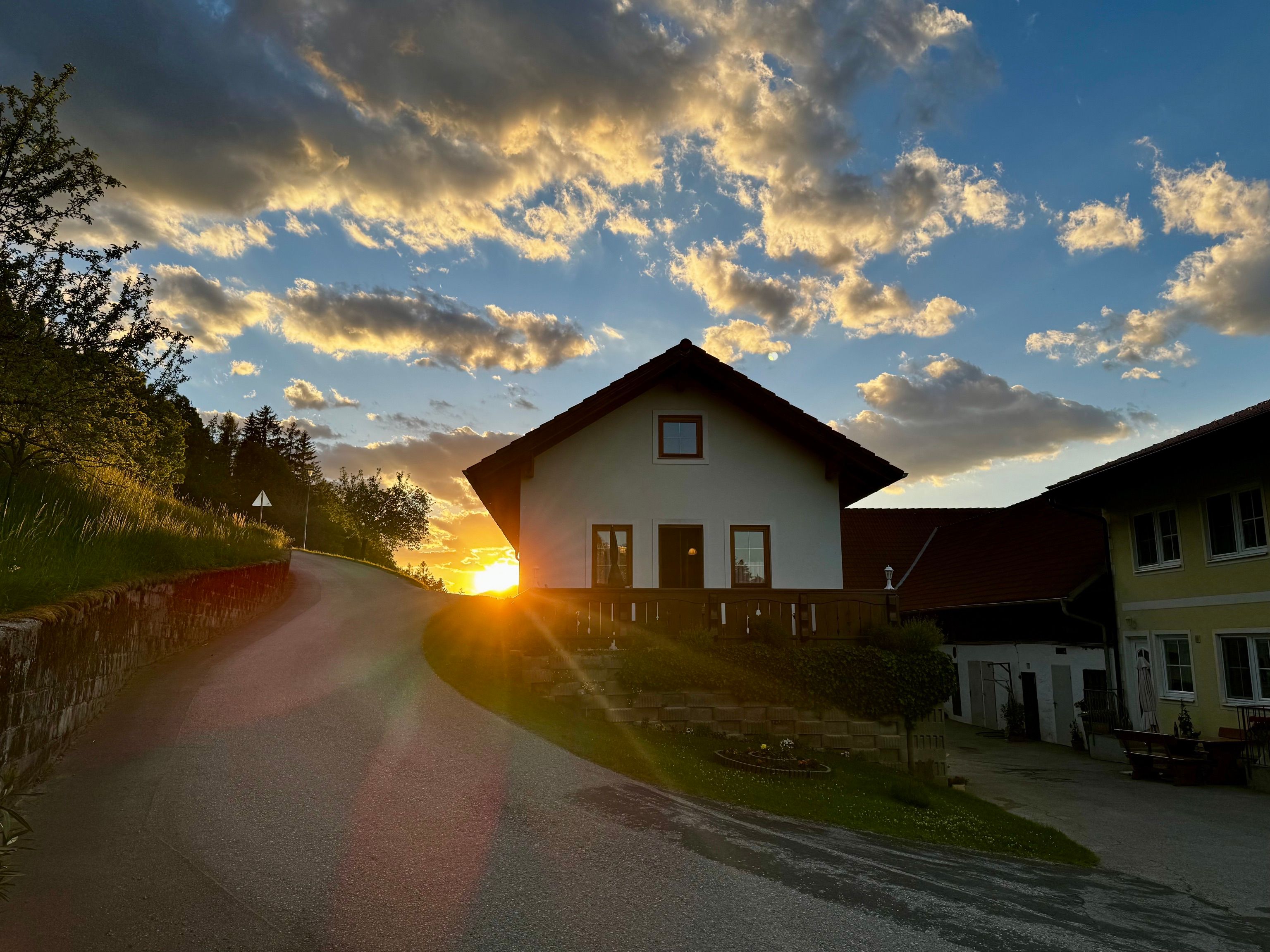 Ein Haus auf einem Hügel bei Sonnenuntergang mit einer kurvigen Straße im Vordergrund.