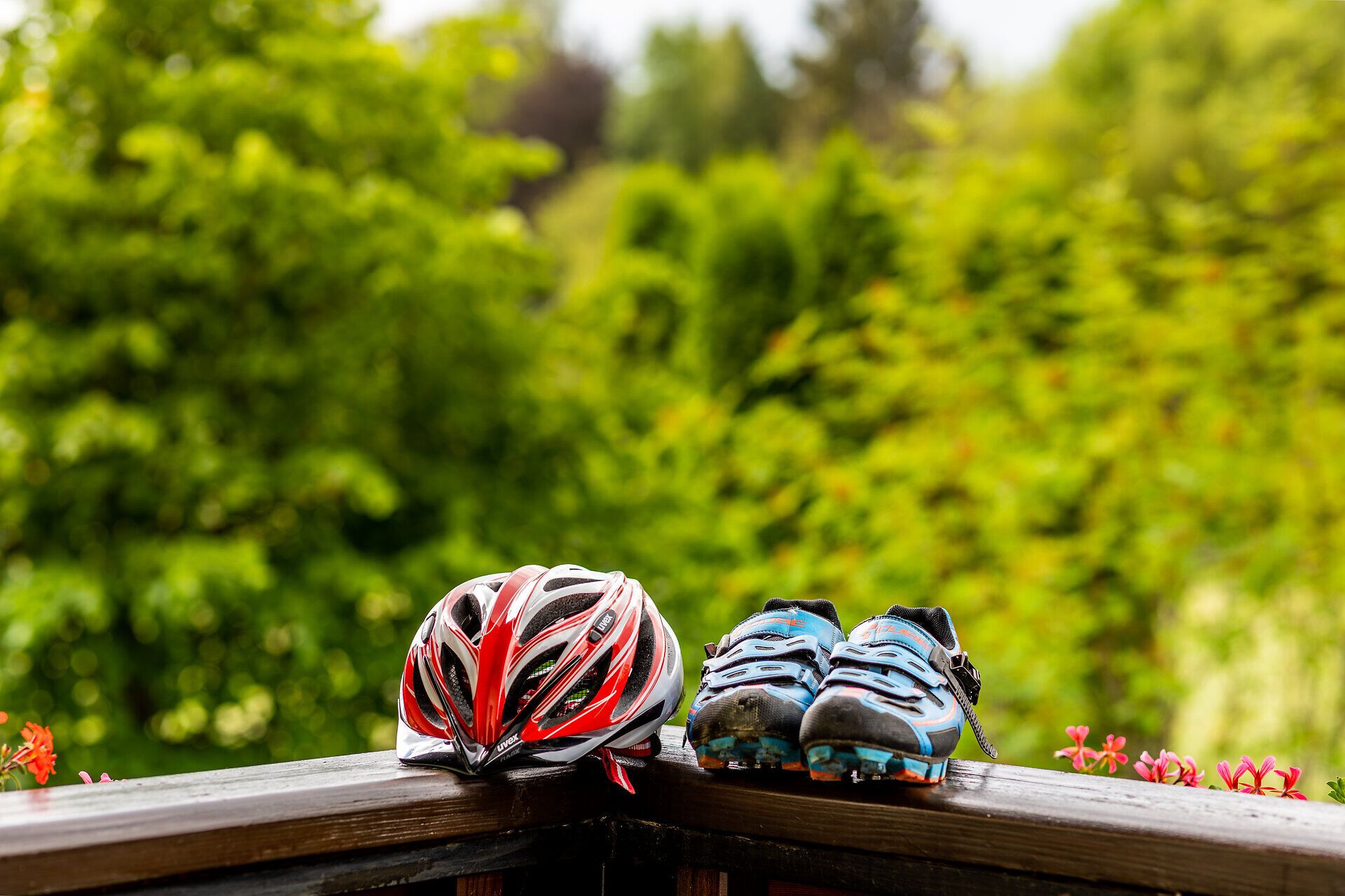 Ein Radhelm sowie Radschuhe wurden auf dem Balkongeländer in der Gasthof Pension St. Wolfgang abgestellt. Vom Balkon aus hat man einen Blick ins Grüne.