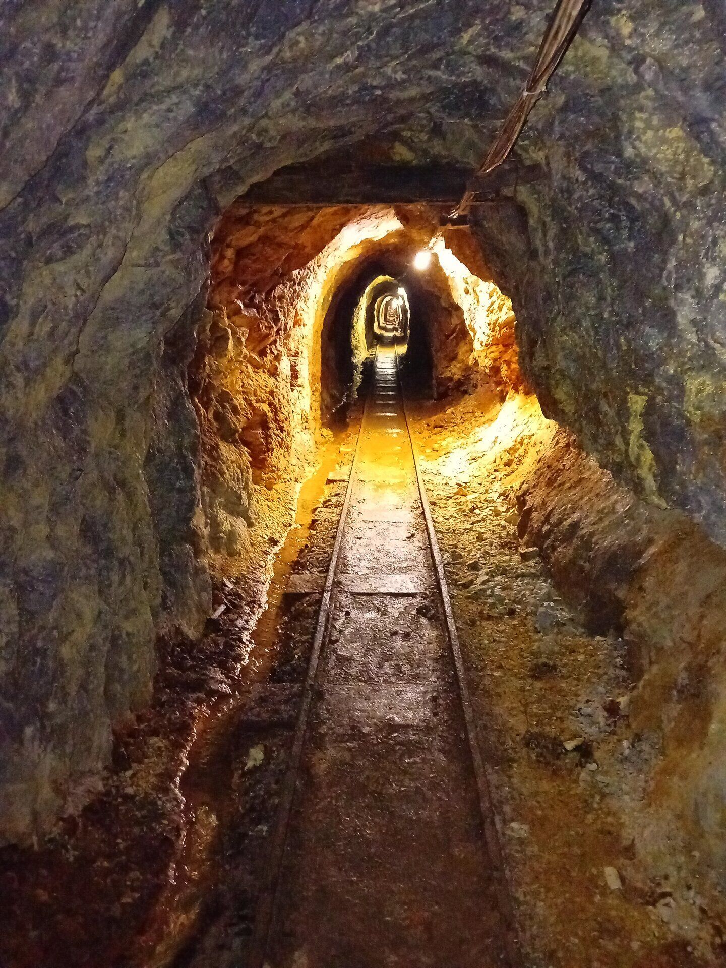Eingang und Innenansicht des historischen Bergwerks „Herlinde Stollen“ mit Schienen und Grubenschild „Glück auf“.
