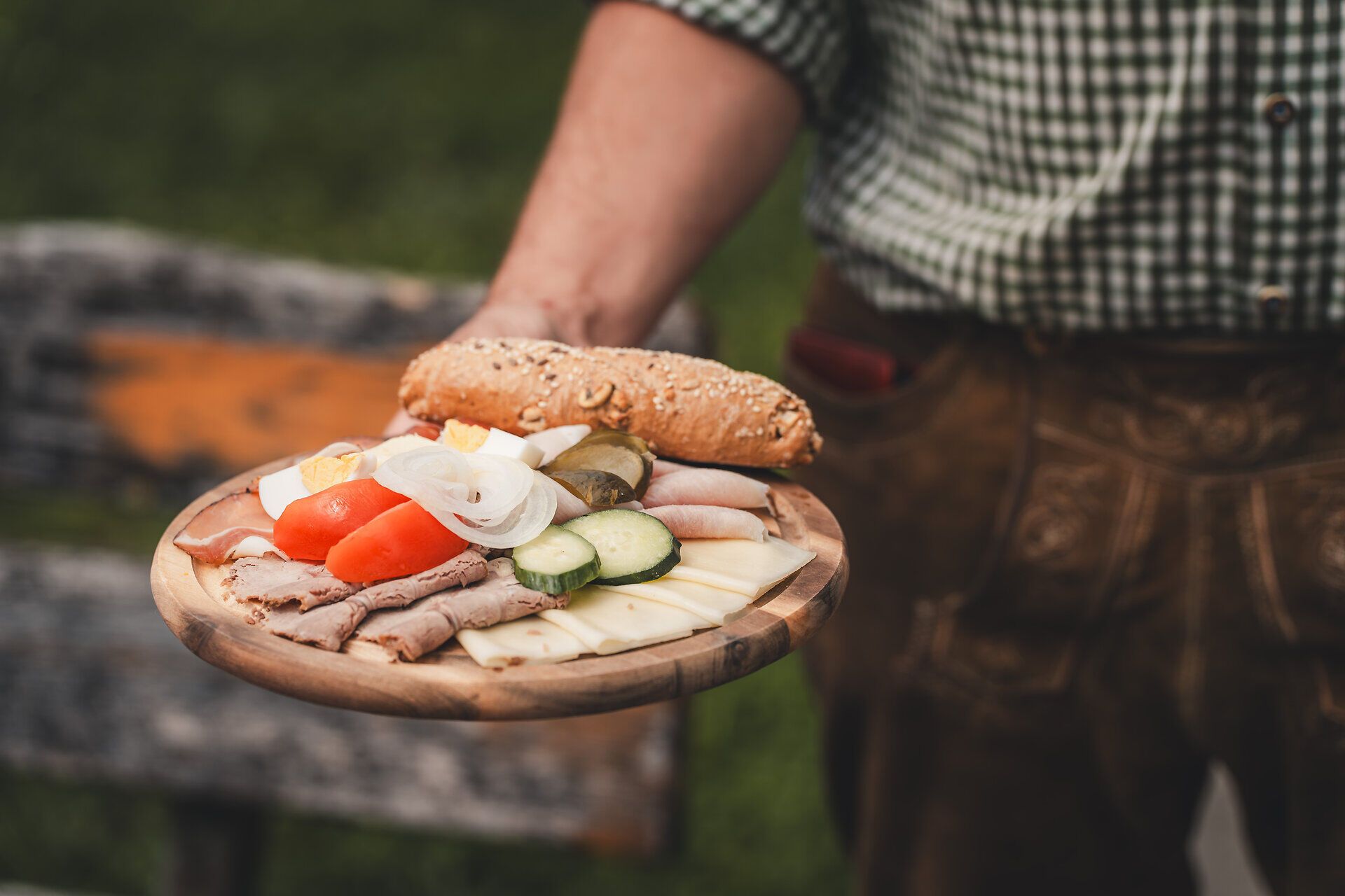 Nahaufnahme einer Mostviertler Jause auf einem rustikalen Holzbrett, präsentiert von einem Mann in Trachtenhemd und Lederhose.