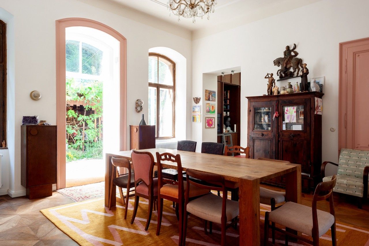 Ein stilvoller Essbereich mit Holztisch, Stühlen und antikem Schrank, dekoriert mit Skulpturen und Gemälden. Große Fenster lassen viel Licht herein.