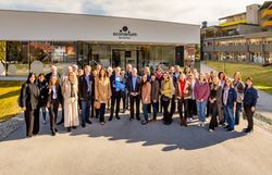 Rund 40 Personen stehen bei Sonnenschein am Vorplatz eines modernen Gebäudes (dem Kulturhaus) mit Glasfront und der Aufschrift "Sconarium Bad Schönau". Der Bürgermeister der Gemeinde Bad Schönau hält ein Logoschild in den Händen.