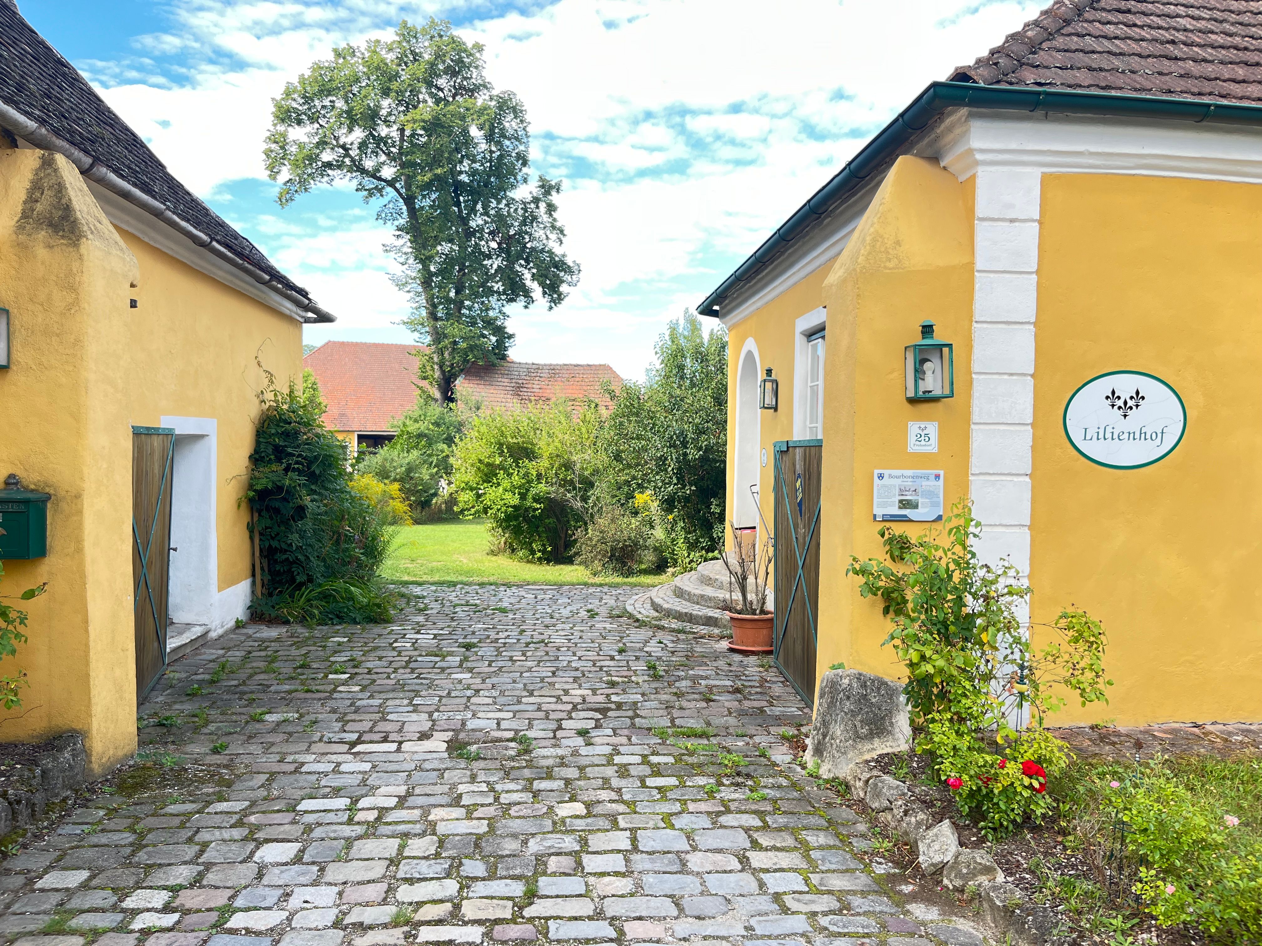 Eingang zum Lilienhof mit gelben Gebäuden und Kopfsteinpflaster.