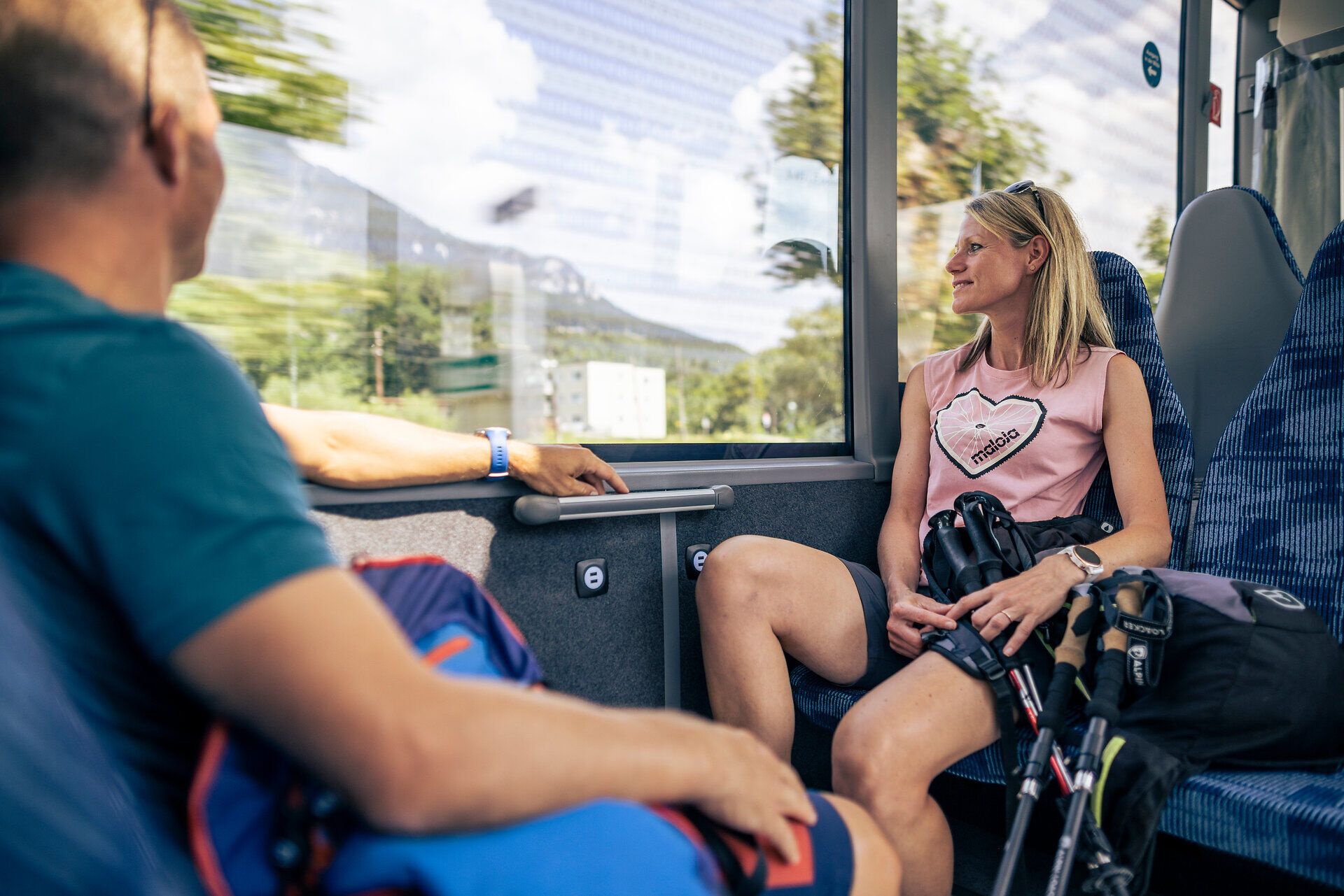Frau sitzt im Bus mit Wanderrucksack und blickt auf die Berge außerhalb des Fensters.