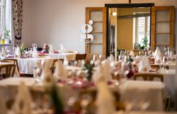 Gaststube im Gasthaus Stocker mit vielen gedeckten Tischen zur Veranstaltung Gedanken-Gänge. An der doppelflügigen Tür hängt ein kleines G, das Logo der Veranstaltung.
