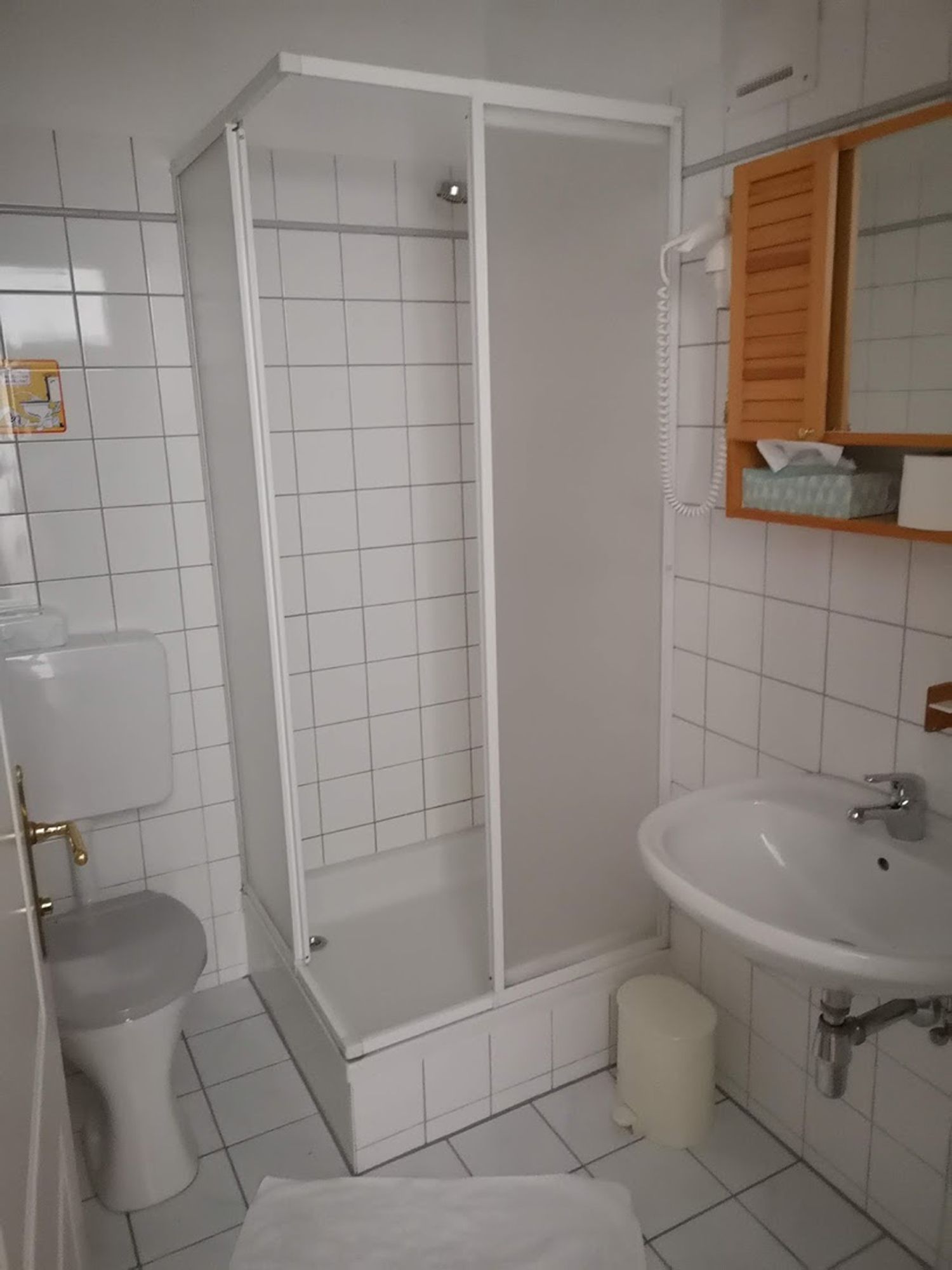 Ein kleines, weiß gefliestes Badezimmer mit Dusche, Toilette und Waschbecken.