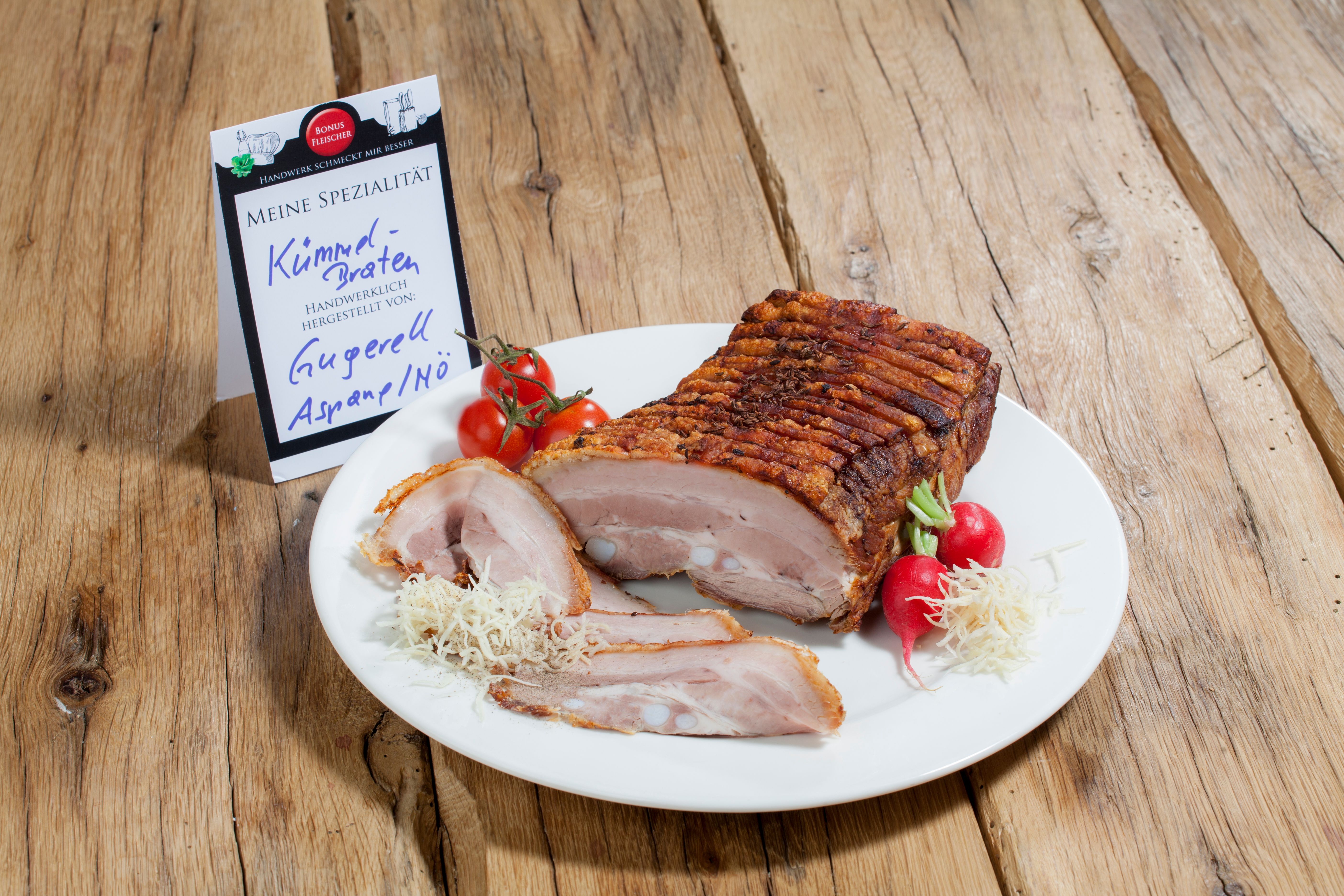 Ein Teller mit Kümmelbraten, Radieschen und Tomaten auf einem Holztisch.
