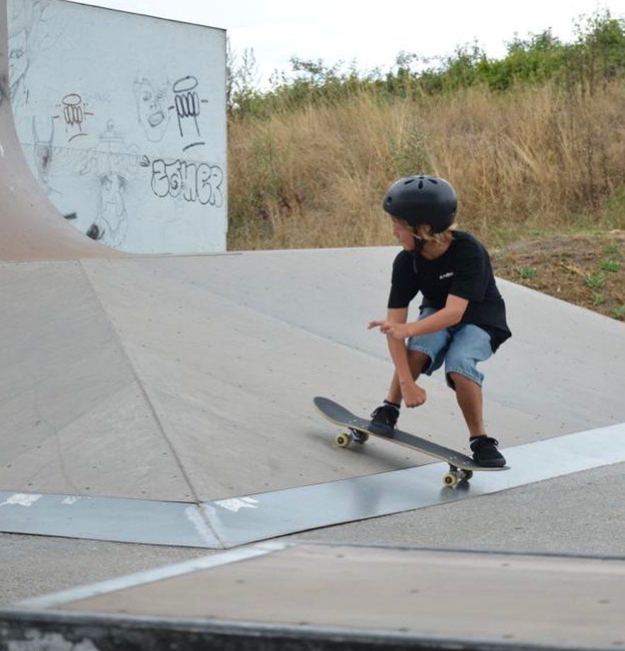 Ein Kind mit Helm fährt auf einem Skateboard in einem Skatepark.