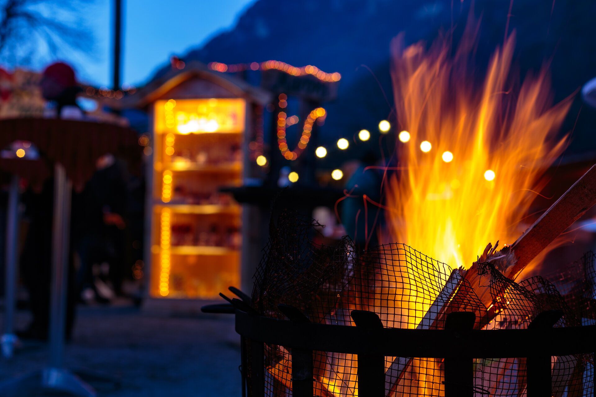Adventmarkt im Schloss Reichenau an der Rax. Das Schloss ist von außen stimmungsvoll beleuchtet, im Innenhof stehen die Hütten. Menschen stehen davor und trinken Punsch.