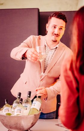 Junger Mann präsentiert den "Wiener-Neustadt"-Wein. Er trägt ein rosa Sakko. 
